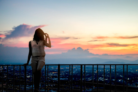 silhouette of beautiful woman standing on the top of town at sunsetの写真素材