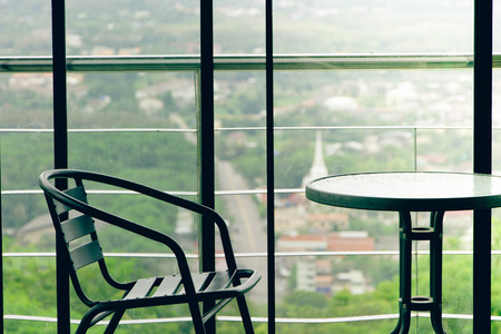 black metal table and chair near the window with blur background of city and green natureの写真素材