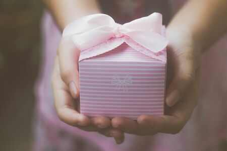 Close up of female hands holding a small pink gift wrapped with pink ribbon