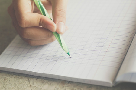 hand with green pen writing on book