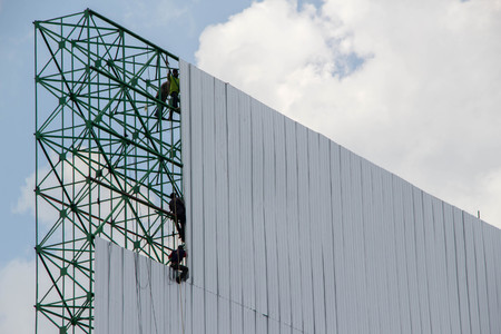 workers installing metal sheets on big billboard with background of blue sky and white cloudの写真素材