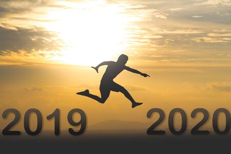 2020 New year concept : Silhouette man jumping from year 2019 to new year 2020  on beautiful gold sky at sunset over mountainの写真素材