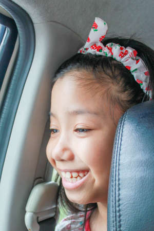 happy and funny Asian young girl with headband smiling in carの写真素材
