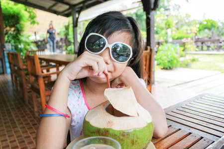 cute Asian girl with sunglasses drinking coconut water in restaurantの写真素材