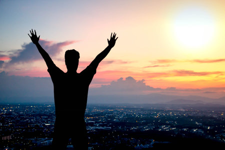 silhouette of man raising hands on top hill to show success or vitory