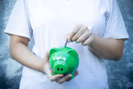 female hand putting coin in green piggy bank