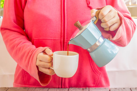 Woman in pink sweater pouring coffee from Moka Pot : vintage coffee makerの写真素材