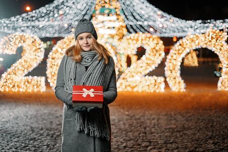 Girl holding gift box on winter festival. Celebrate New Year EVE 2020. Against a background the...