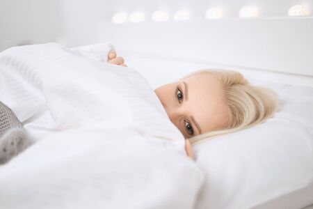 Natural beautiful woman laying in the bed. Girl hiding behind a blanket.の写真素材