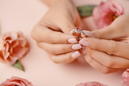 Close up of woman's hand holding elegant diamond ring with feather and pink background with flowers....