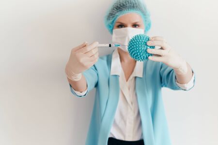 Woman in a protective mask holds an injection syringe and symbol of coronavirus. Biological hazard.の写真素材