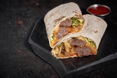 Wrap with beef, vegetables and ketchup isolated on dark wood  background. Closeupの写真素材