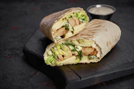 Wrap with fried chicken, vegetables and sauce isolated on dark wood  background. Closeupの写真素材