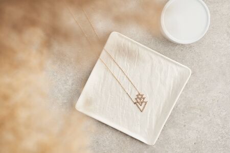 Modern minimalist geometric golden necklace on white marble plate . Necklace in the form of three triangles. Women accessories.の写真素材