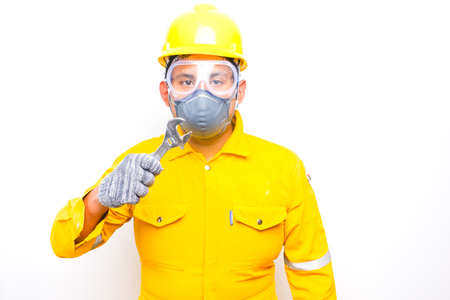 A picture of men wearing cover all, eye protector, safety helmet, face mask and gloves holding wrench.の写真素材