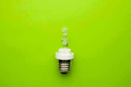 A picture of broken E27 type modelling light bulb on green background without glass. Green energy...