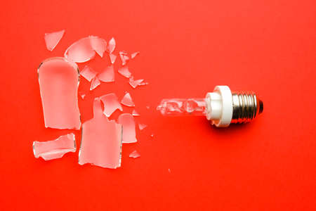 A picture of broken E27 type modelling light bulb on red background.