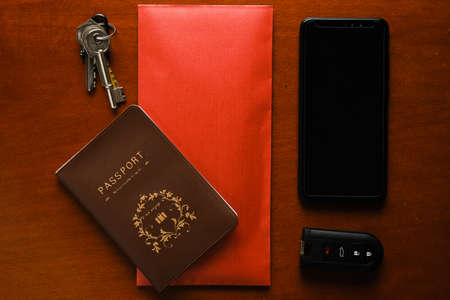 A flatlay picture of bribery gift concept using copyspace red envelope money inside, blank smartphone, remote car key, house key, miniature and passport. International Anti-Corruption Day concept.の写真素材