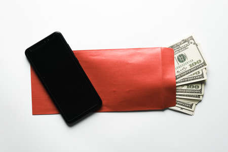 A picture of blank smartphone on the envelope filled of fake money on white table. International Anti-Corruption Day concept.の写真素材