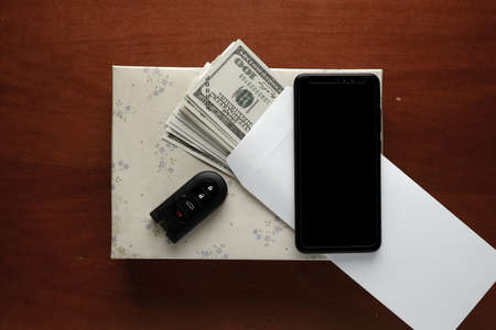 Flatlay picture of fake money in envelope, smartphone, car key and gift box on the table. Corruption...