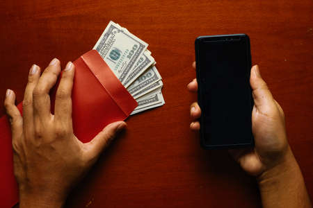 Dramatic picture of hand holding envelope with fake money and copyspace smartphone for corruption...