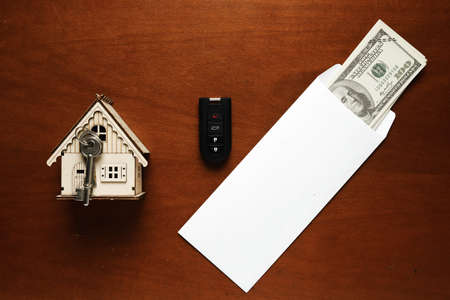 Flatlay picture of envelope contain money, car key, house key and miniature on the table. Variety...