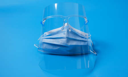 A picture of face shield and face maskon blue background. Face shield is needed and advised to wear...
