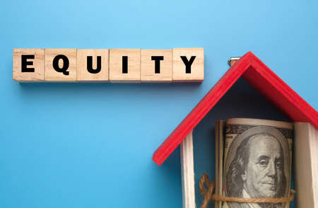 A picture of wooden block with Equity word, house miniature and fake money insight. Equity is the difference between the market value of your home and the amount you owe the lender who holds the mortgageの写真素材