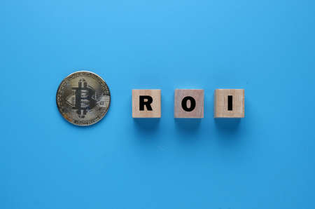 A picture of Bitcoin coin and ROI on wooden block. ROI at Bitcoin now questionableの写真素材
