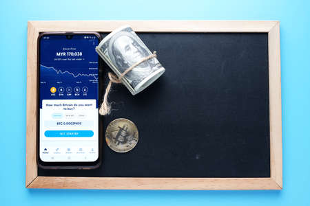 "Kuala Lumpur, Malaysia- Circa May, 2021: Famous crypto mobile apps, Luno at smartphone, Bitcoin and Fake cash on copyspace blackboard.のeditorial素材