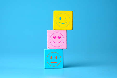 A picture of winking, love and neutral emoticon at wooden block on blue backgroundの写真素材