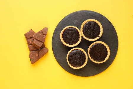 A picture of 4 chocolate tart on slate plate bar on yellow background. Food prepared for dessert.の写真素材
