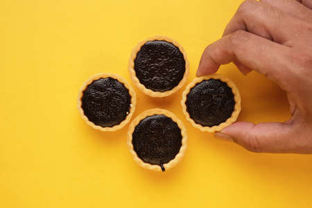 A picture of hand taking homemade chocolate tart on yellow background. Same colour subject and background conceptの写真素材