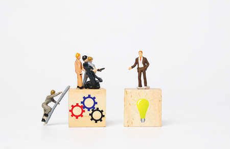 A picture of miniature in coat on bulb wooden block as thinker. Worker miniature on gear wooden block as executor. Thinker and worker achieve the company vision.の写真素材