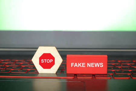 A picture of stop sign on hexagon wood cut and fake news at red wood on laptop keyboard. Stop fake news conceptの写真素材
