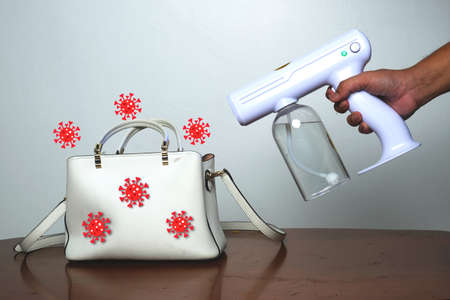 A picture of hand holding wireless rechargeable nano blue ray atomizer spray gun sanitizing a handbagの写真素材