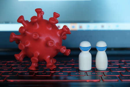 A picture of coronavirus and natural wooden people wearing face mask on laptop keybord. Save workplace from Covid-19.の写真素材
