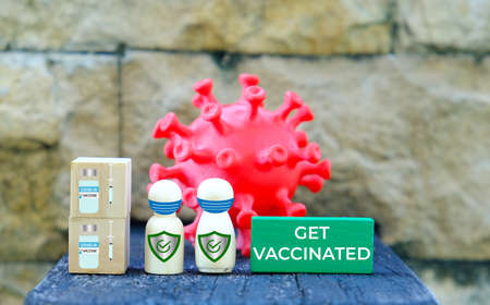 A picture of coronavirus and natural wooden people wearing face mask on wooden block with 2 doses covid-19 vaccine and get vaccinated word.の写真素材