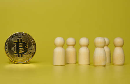 Wooden figures of people and bitcoin on a yellow background. The concept of crypto currency.