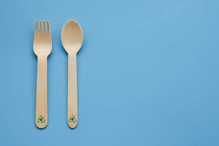 A picture of cross wooden fork and spoon with recycleable logo insight on copyspace blue background. Recyleable, eco-friendly and plastic free material used in food industry.の写真素材