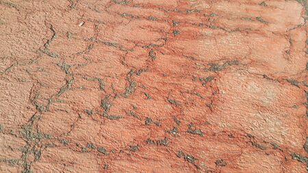Red colored damaged road or paved pathway with crackes of different shpaes. Cracked texture with...