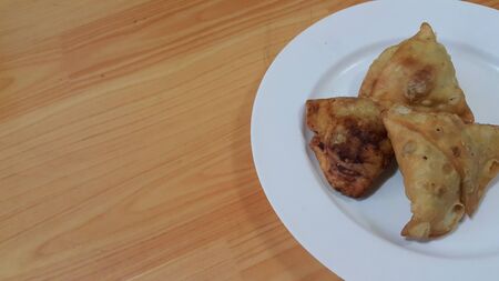 Closeup of delicious home made spicy and crunchy samosa pastries placed in a white ceramic plate on wooden floorの写真素材