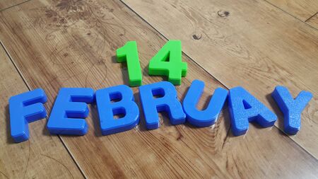 Plastic colored alphabets making words 14 February are placed on a wooden floor. These plastic...