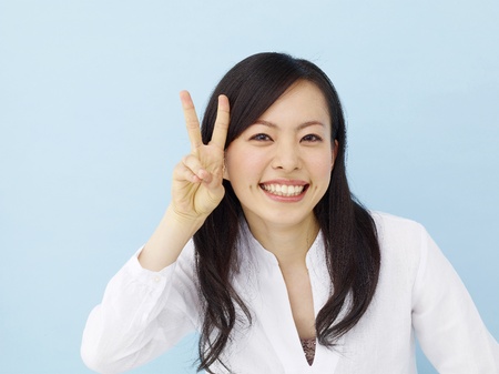 Happy young japanese girl showing victory sign isolated on blue backgroundの写真素材
