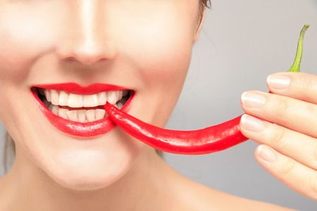 Beautiful woman teeth eating red pepperの写真素材