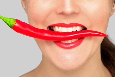 Beautiful woman teeth eating red pepperの写真素材