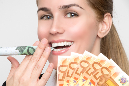 Beautiful laughing woman smokes a rolled-up 100 Euro banknote and holds 50 Euro notes fanned in the handの写真素材