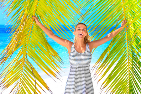 Gorgeous laughing blond woman with dress and coconut in hand at the palm tree at the beachの写真素材