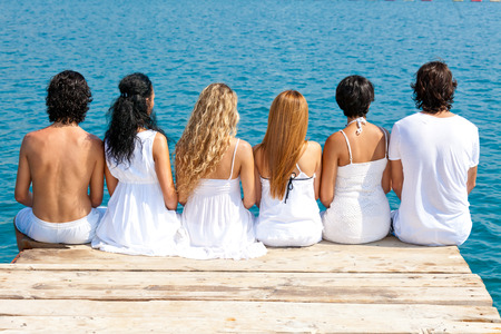 Women and men from behind sit side by side on the wooden walkwayの写真素材