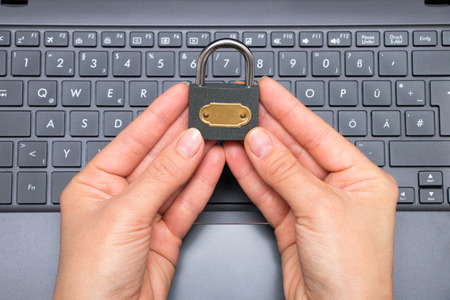 Woman holds a locked padlock between her fingers over a laptopの写真素材